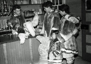 Johnnie, his wife and child with George Anderson examining white fox pelts at the Hudson's Bay Company store. (Photo credit: Arthur H. Tweedle / Library and Archives Canada / e002344213)